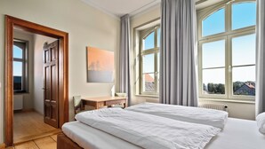 A hotel room with a large bed, a desk, a chair, and a window with curtains. - Villa Bianca am Huy (Huy)