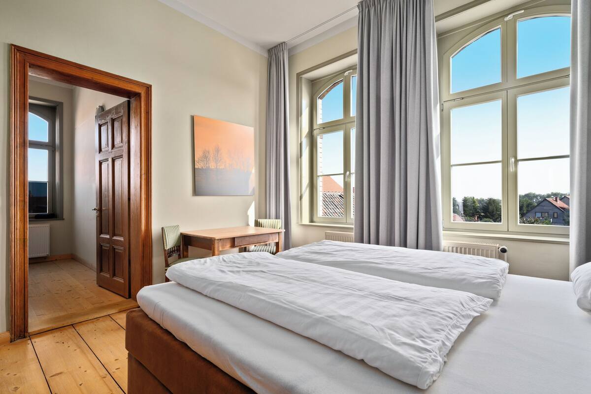 A hotel room with a large bed, a desk, a chair, and a window with curtains.