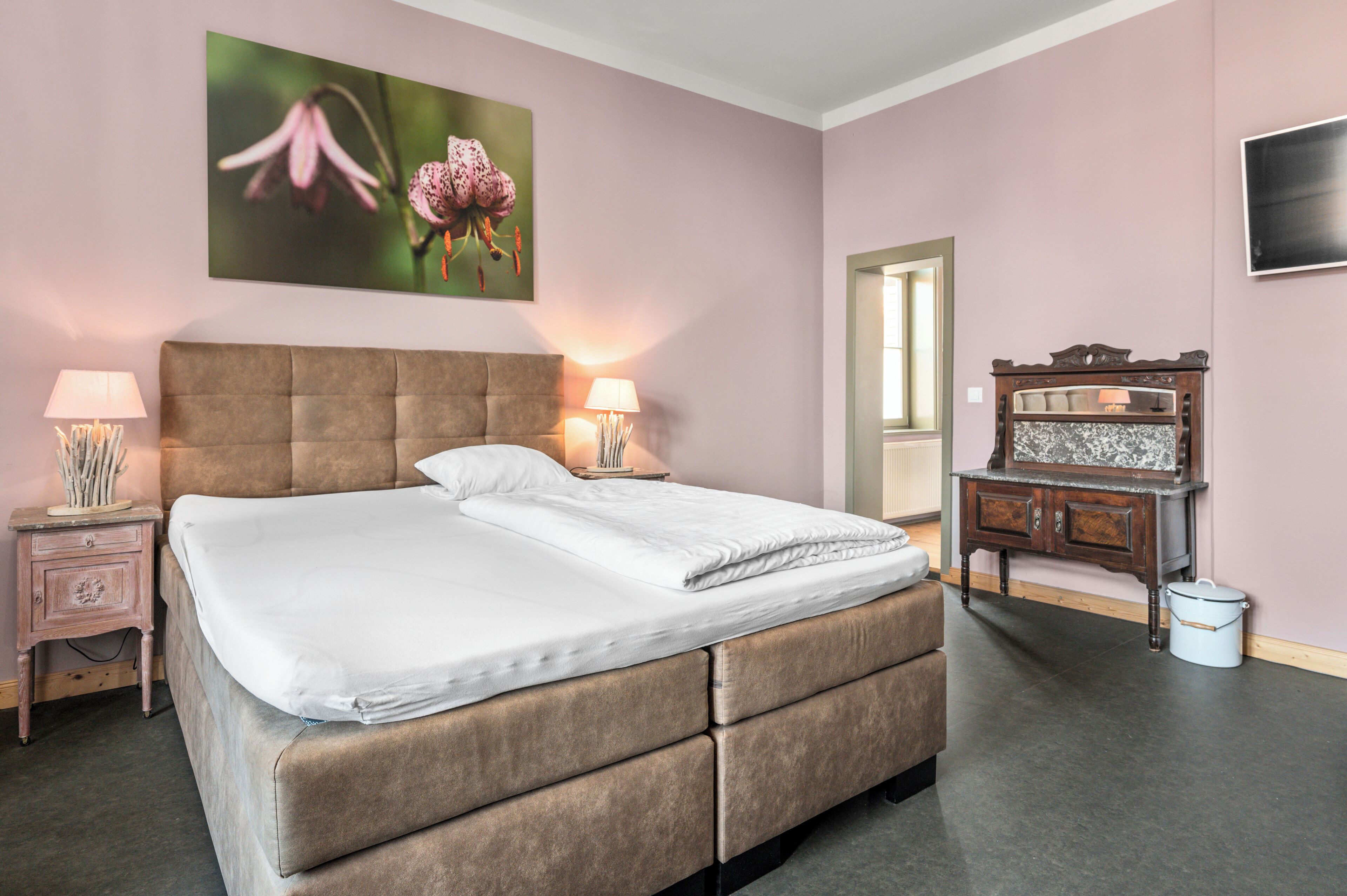 Un dormitorio con una cama grande, dos mesitas de noche con lámparas, un aparador y un cuadro en la pared.