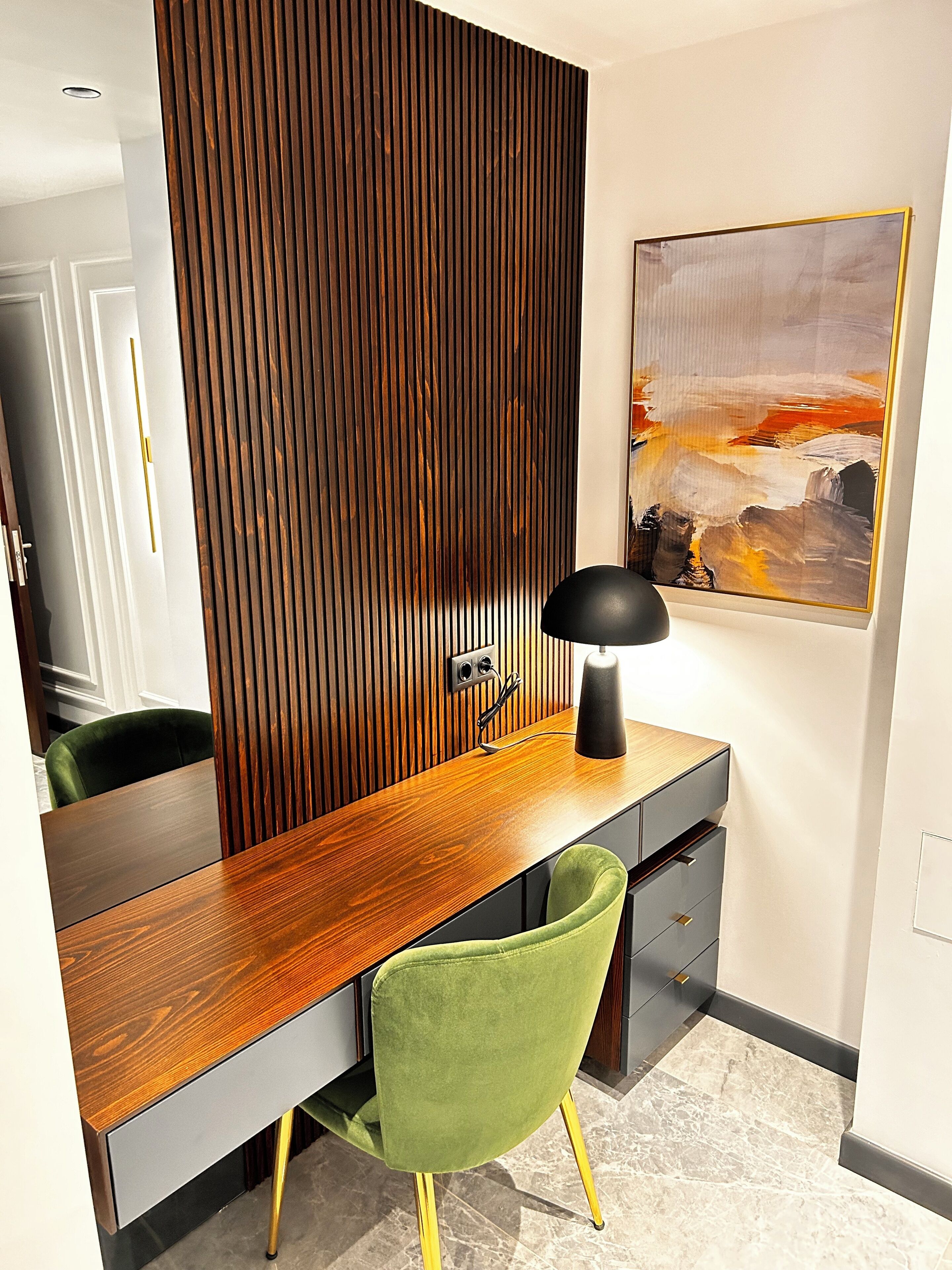 Un espace de bureau moderne avec un bureau en bois, une chaise verte, une lampe noire et un tableau accroché au mur.