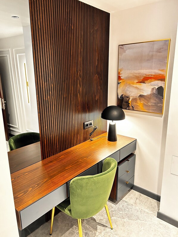 Un espace de bureau moderne avec un bureau en bois, une chaise verte, une lampe noire et un tableau accroché au mur.