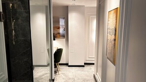Un pasillo con una puerta de cristal que da a un baño, una silla y un cuadro en la pared.