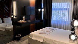 Una habitación de hotel moderna con una cama grande, un escritorio, un televisor y una ventana con cortinas.