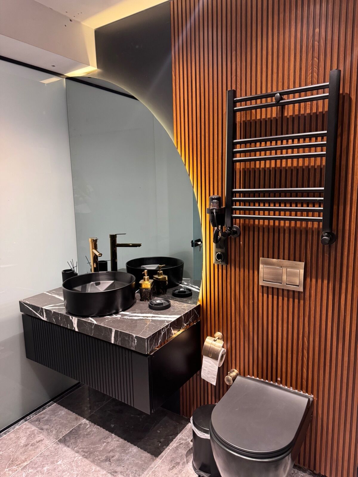 Une salle de bain moderne avec un meuble-lavabo aux lignes courbes, un évier noir et un mur recouvert de panneaux en bois.