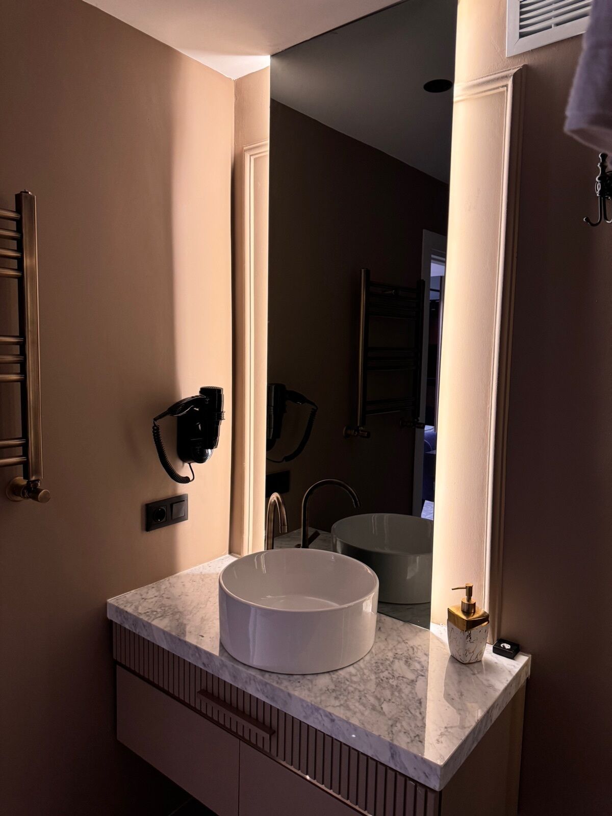 A modern bathroom with a large mirror, a white sink, and a towel rack.