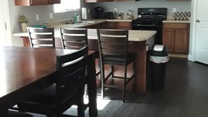 A modern kitchen with wooden cabinets, a central island, and a dining area with chairs. - The Zion Getaway-Located in beautiful Southern Utah (La Verkin)