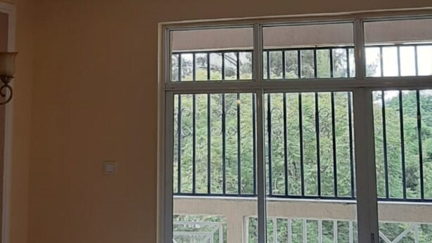 A room with a large window, a sofa with cushions, and a chandelier. - Riverland Apartments (Nairobi)
