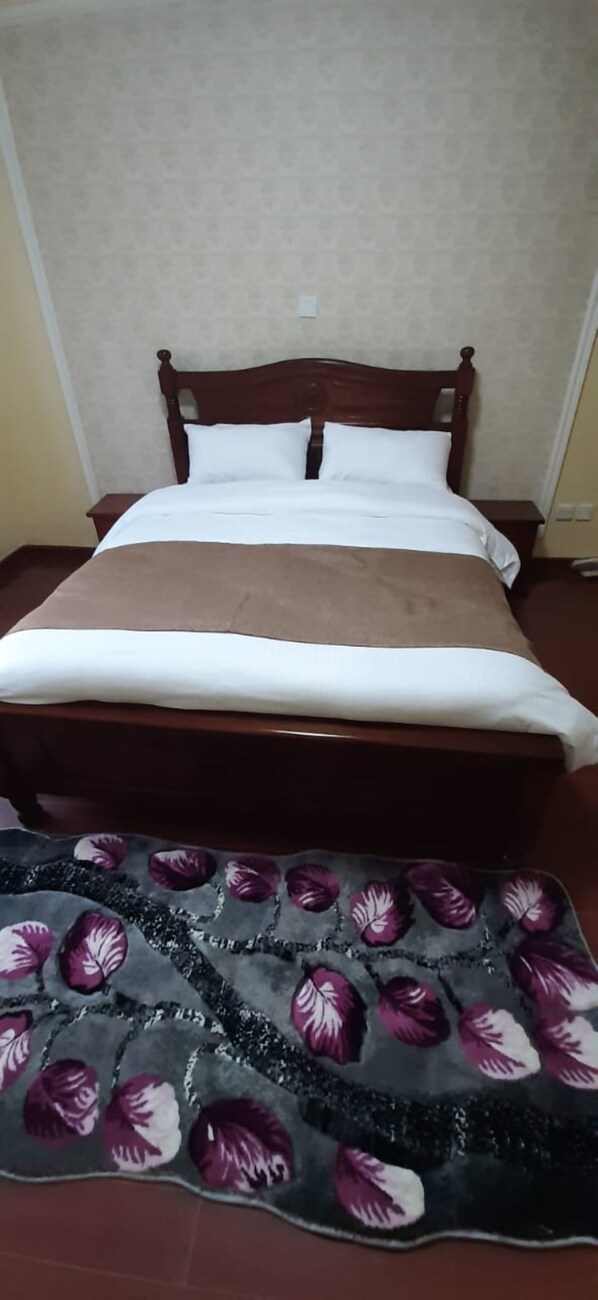 Una cama con cabecera de madera, ropa de cama blanca y una manta marrón.