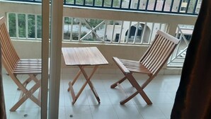 A balcony with two wooden chairs and a small table, a railing, and a view of buildings and greenery. - Riverland Apartments (Nairobi)