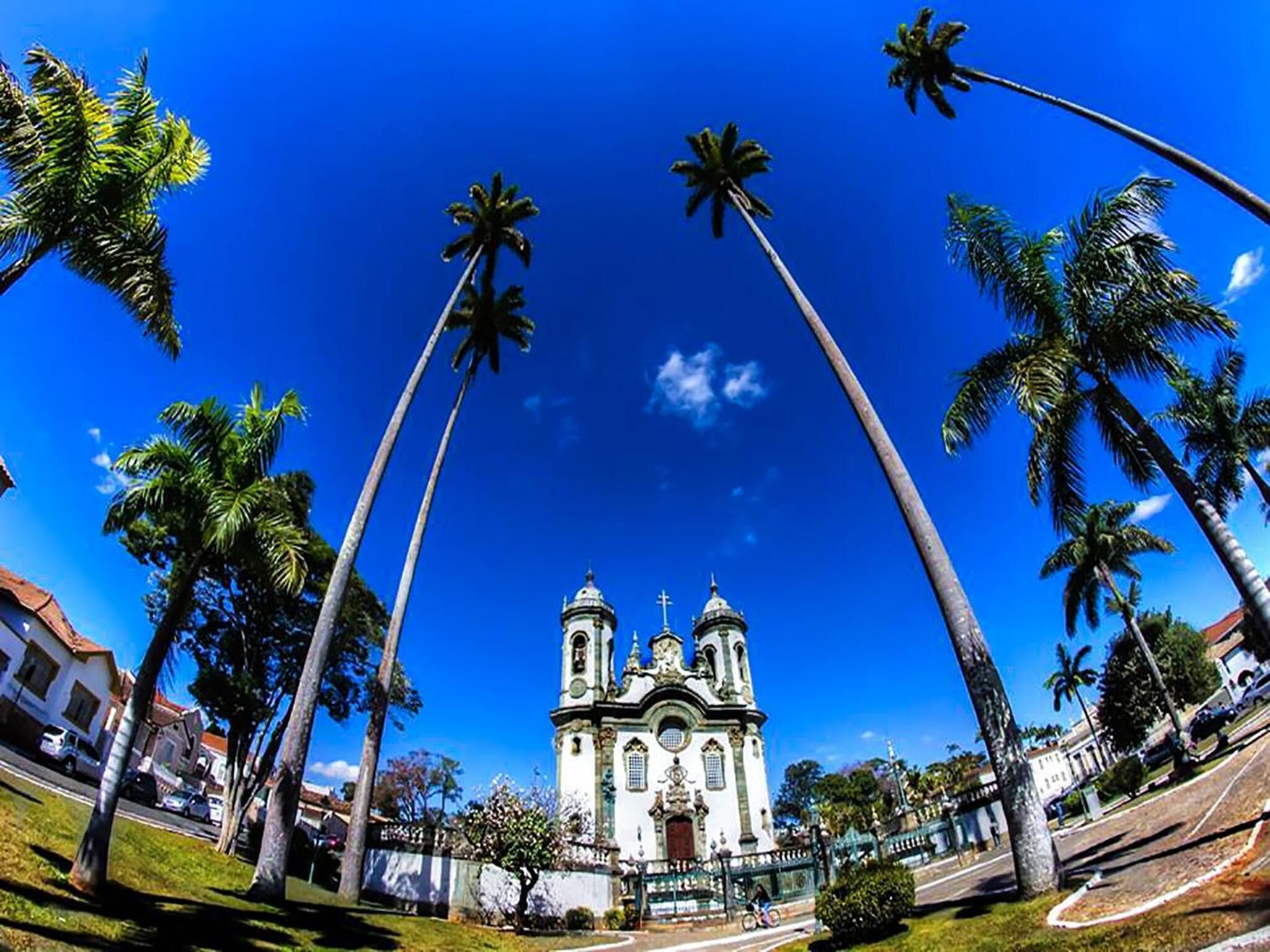Uma igreja com duas torres e uma cúpula central, rodeada por palmeiras e um céu azul límpido.