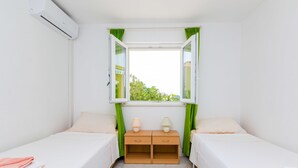 A small, clean room with two single beds, a wooden nightstand with two lamps, and a window with green curtains. - Rooms Villa Bind (Konavle)