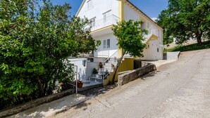 A two-story building with a white facade and yellow trim, a staircase leading to the upper floor, and a small garden area with potted plants. - Rooms Villa Bind (Konavle)