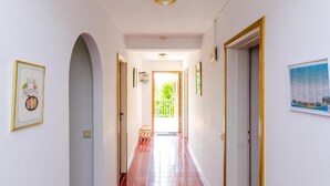 A hallway with a red-tiled floor, white walls, and framed pictures. - Rooms Villa Bind (Konavle)