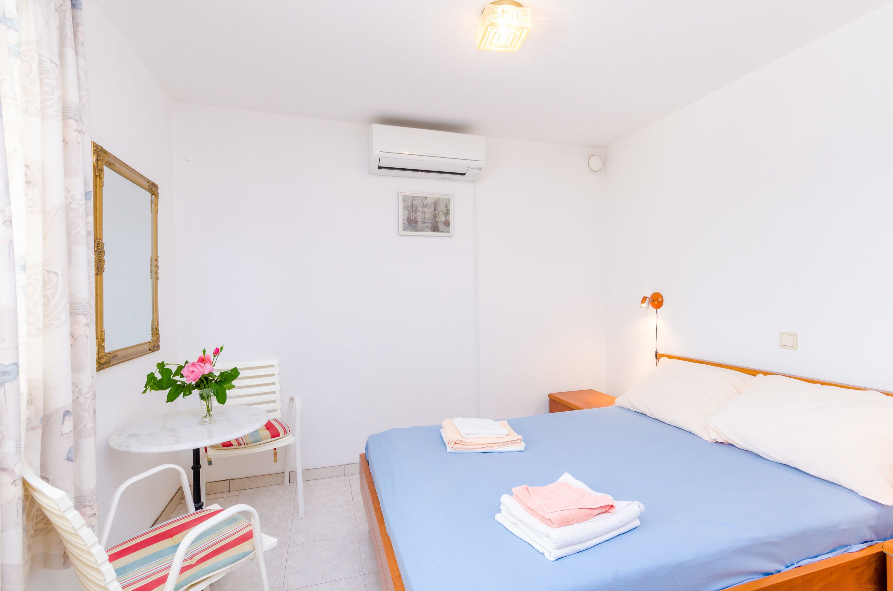 Hotelkamer met een bed, een klein tafeltje met een stoel, een spiegel en een airconditioner.