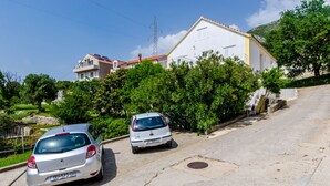 A residential street with two parked cars, a white building with a red roof, and lush greenery. - Rooms Villa Bind (Konavle)