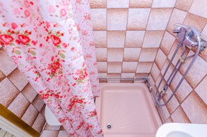 A bathroom with a pink bathtub, floral shower curtain, and tiled walls. - Rooms Villa Bind (Konavle)