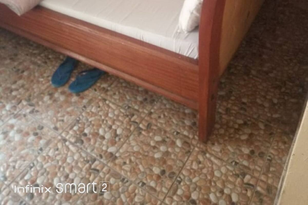A bed with a wooden frame and a floral bedspread, placed on a pebble-patterned floor.
