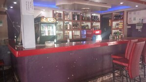 A bar area with a counter, shelves of bottles, and a Coca-Cola refrigerator. - Small Villa Gardens (Kabati)
