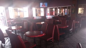 A restaurant interior with red chairs and tables, a television mounted on the wall, and patterned flooring. - Small Villa Gardens (Kabati)