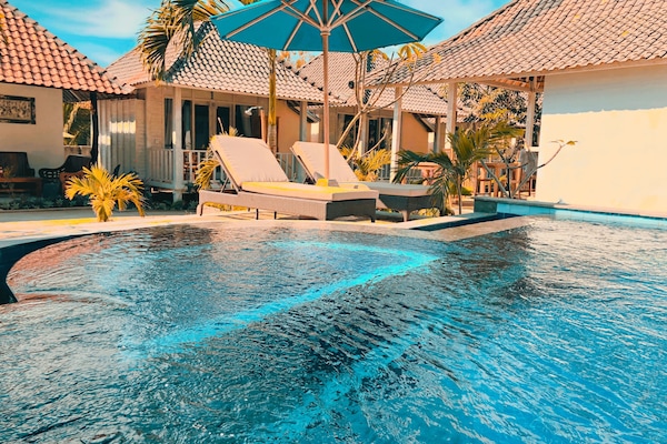 Una piscina al aire libre, sombrillas, sillones reclinables de piscina