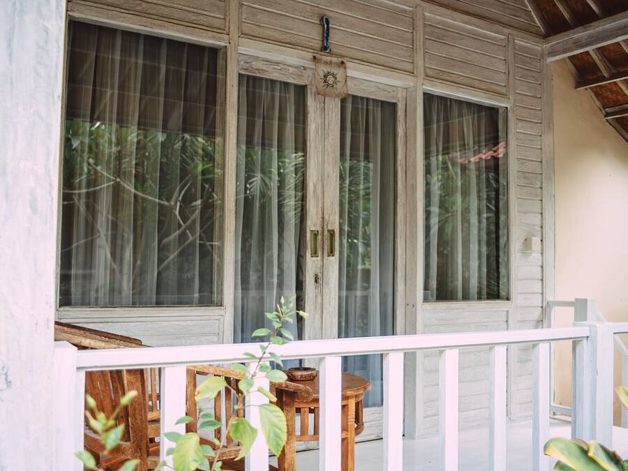 A wooden porch with a white railing, large windows with curtains, and a small table.