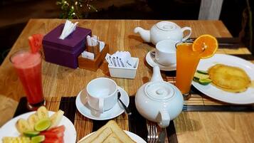 A breakfast setup with a teapot, cups, a glass of orange juice, and plates of toast and fruit.