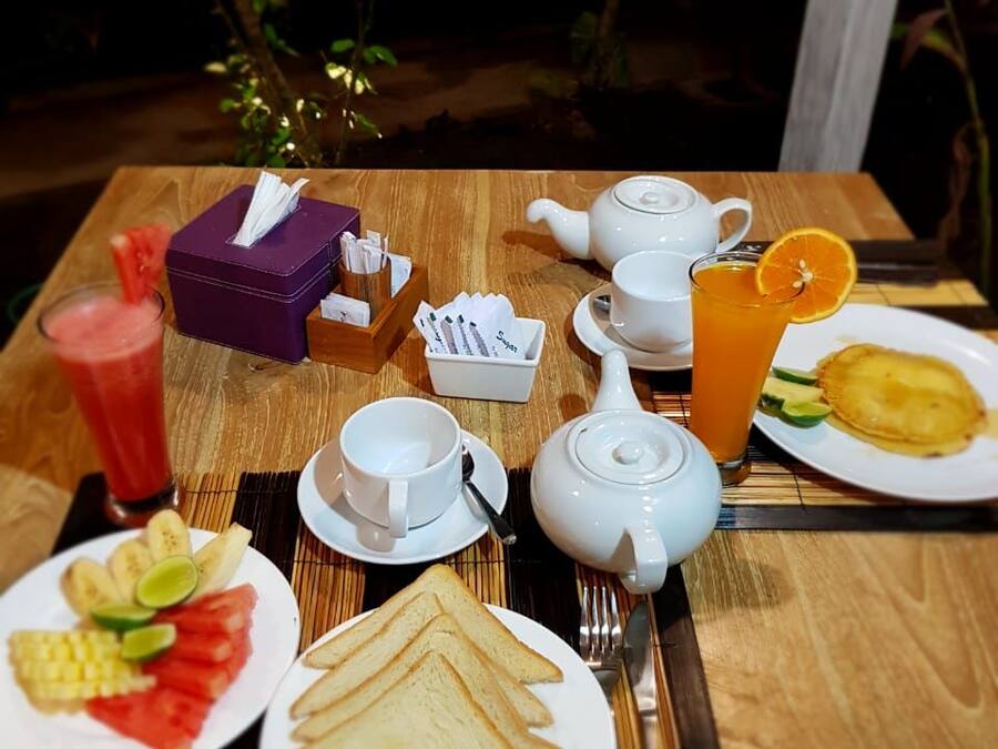 A breakfast setup with a teapot, cups, a glass of orange juice, and plates of toast and fruit.