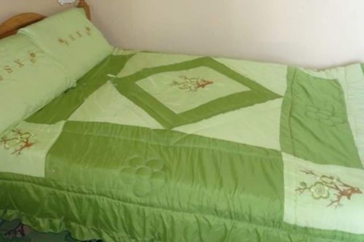 A bed with a green and white quilted bedspread and matching pillows.