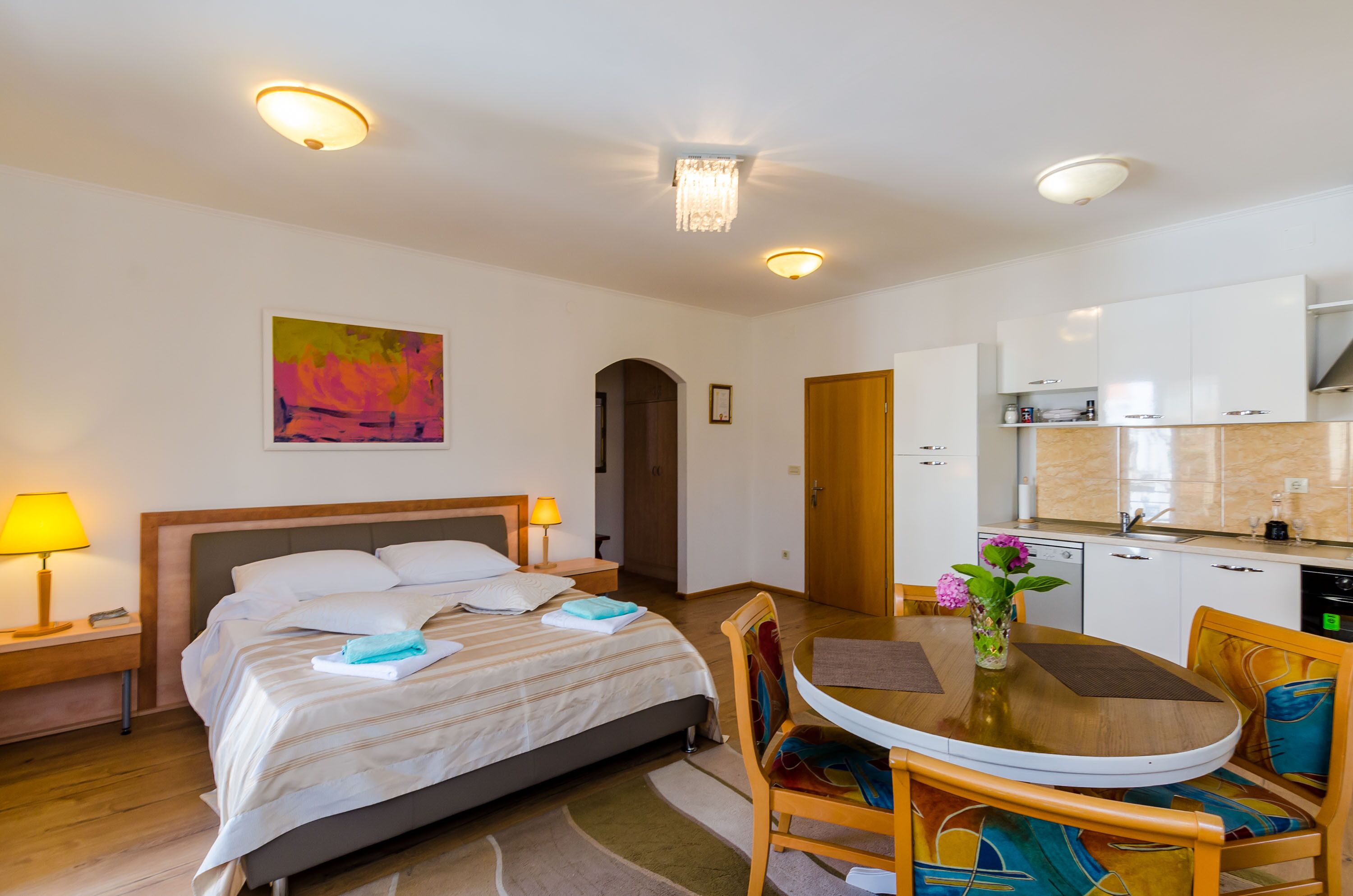 A hotel room with a bed, bedside table, lamp, and a dining area with a table and chairs.