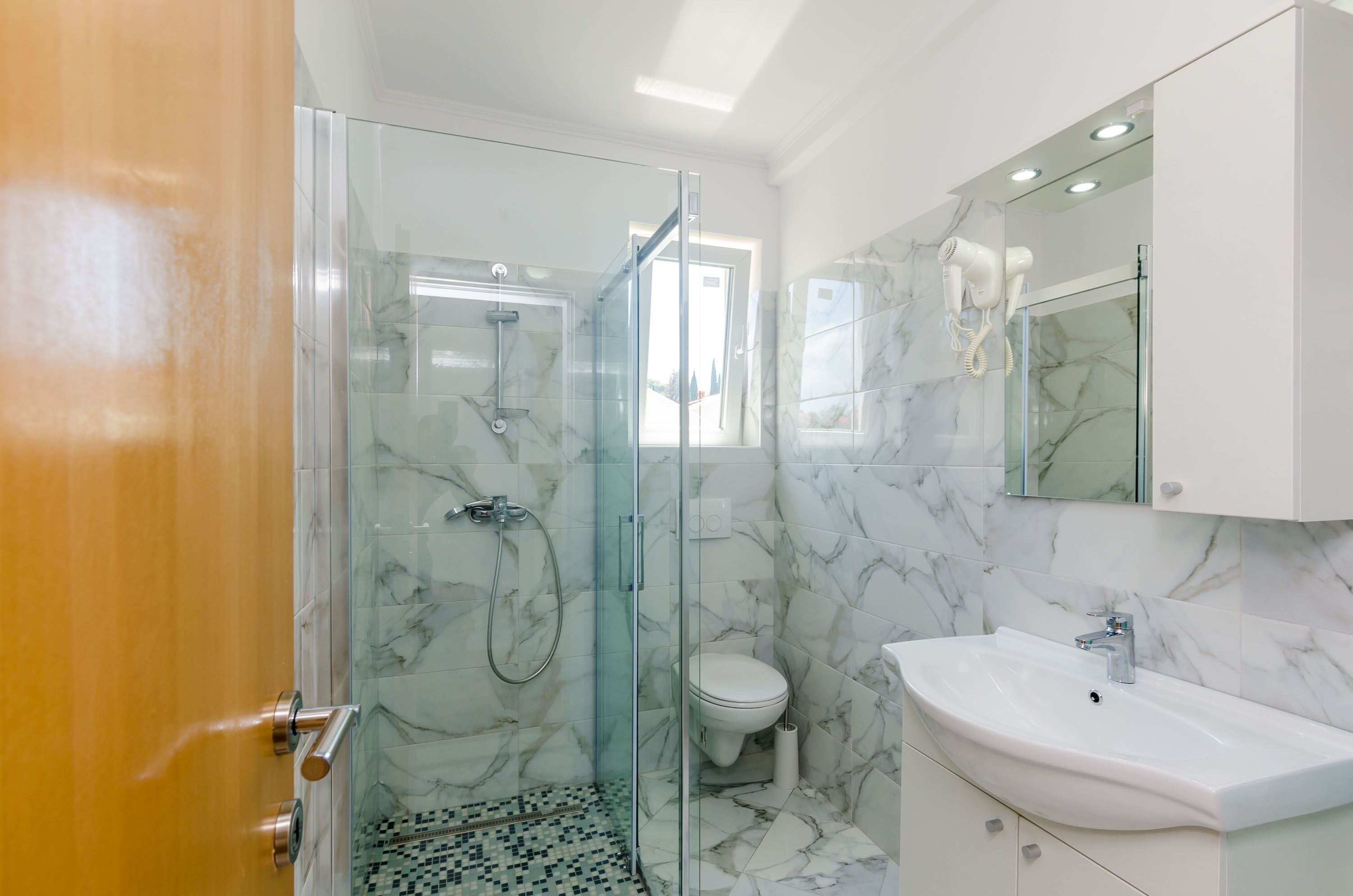 A modern bathroom with a glass-enclosed shower, a white sink, and a marble-tiled floor.