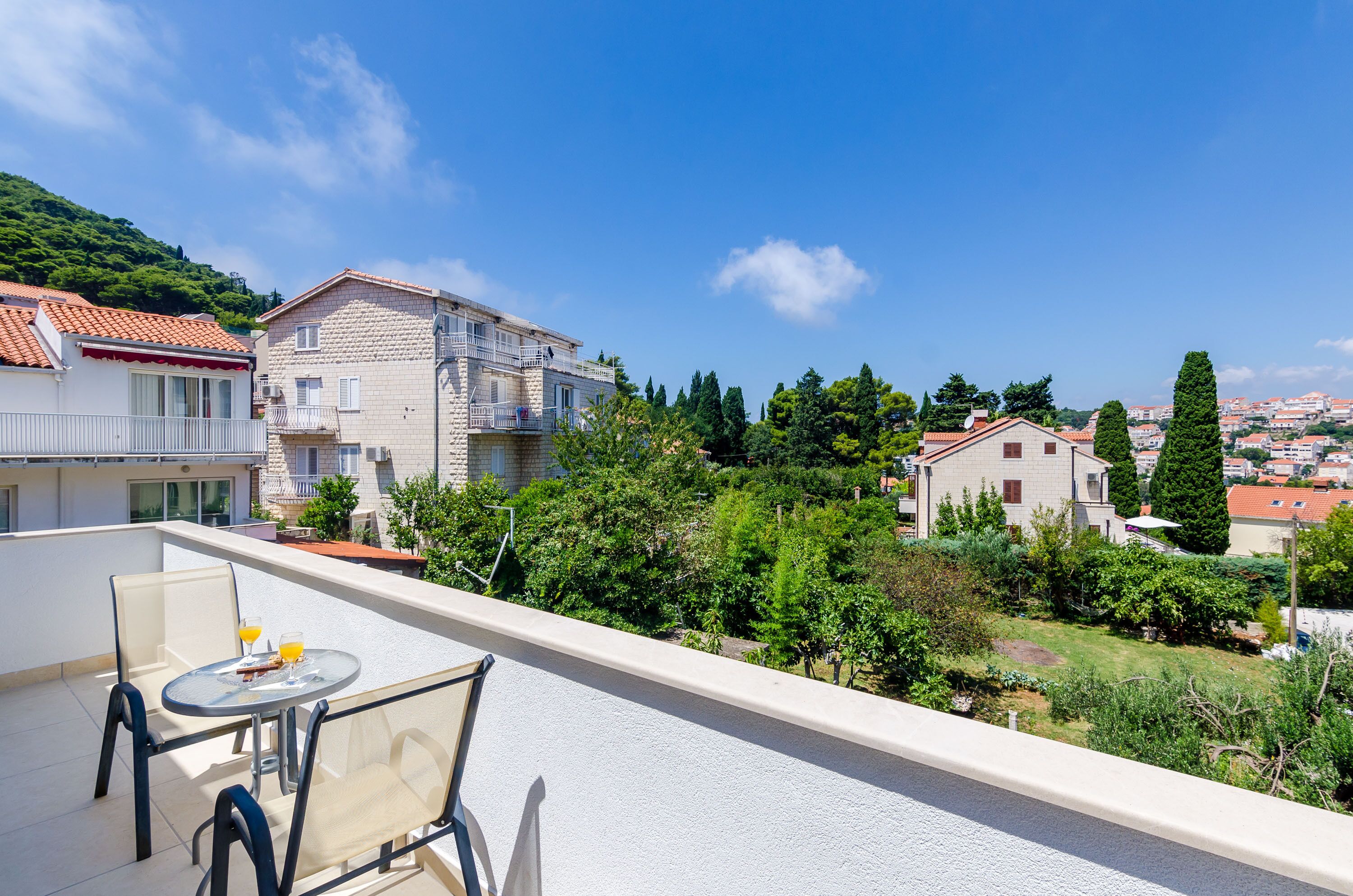 A balcony with a table and chairs, overlooking a residential area with houses and greenery.
