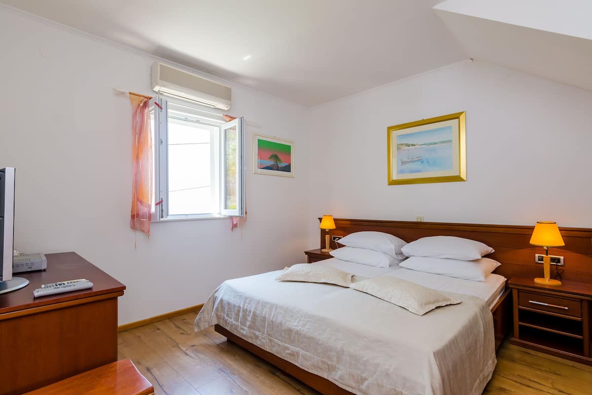 A bedroom with a bed, bedside tables, a desk, a television, and a window with curtains.