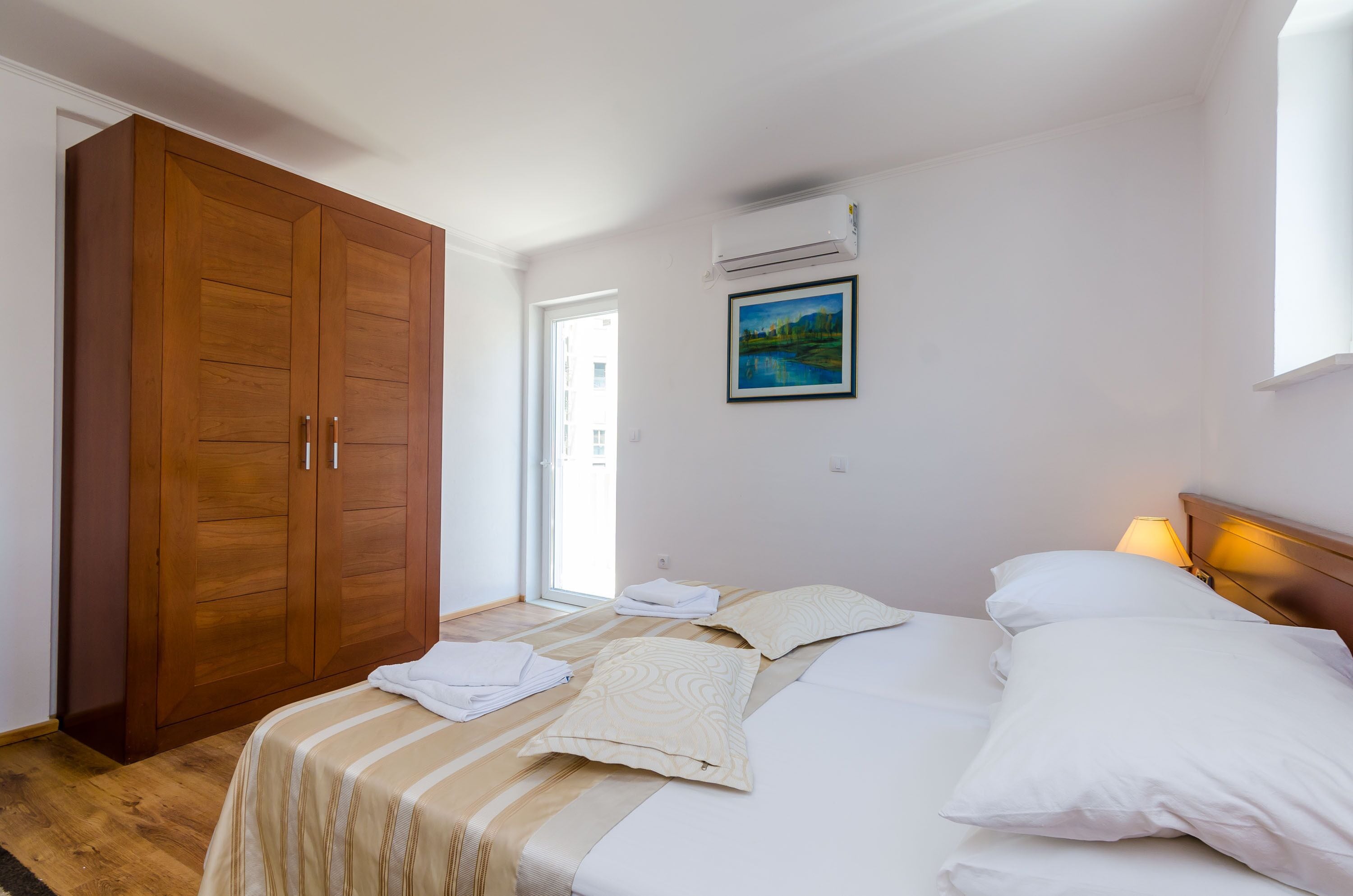 Une chambre à coucher avec un lit, des oreillers, une armoire en bois, un tableau et un appareil de climatisation.
