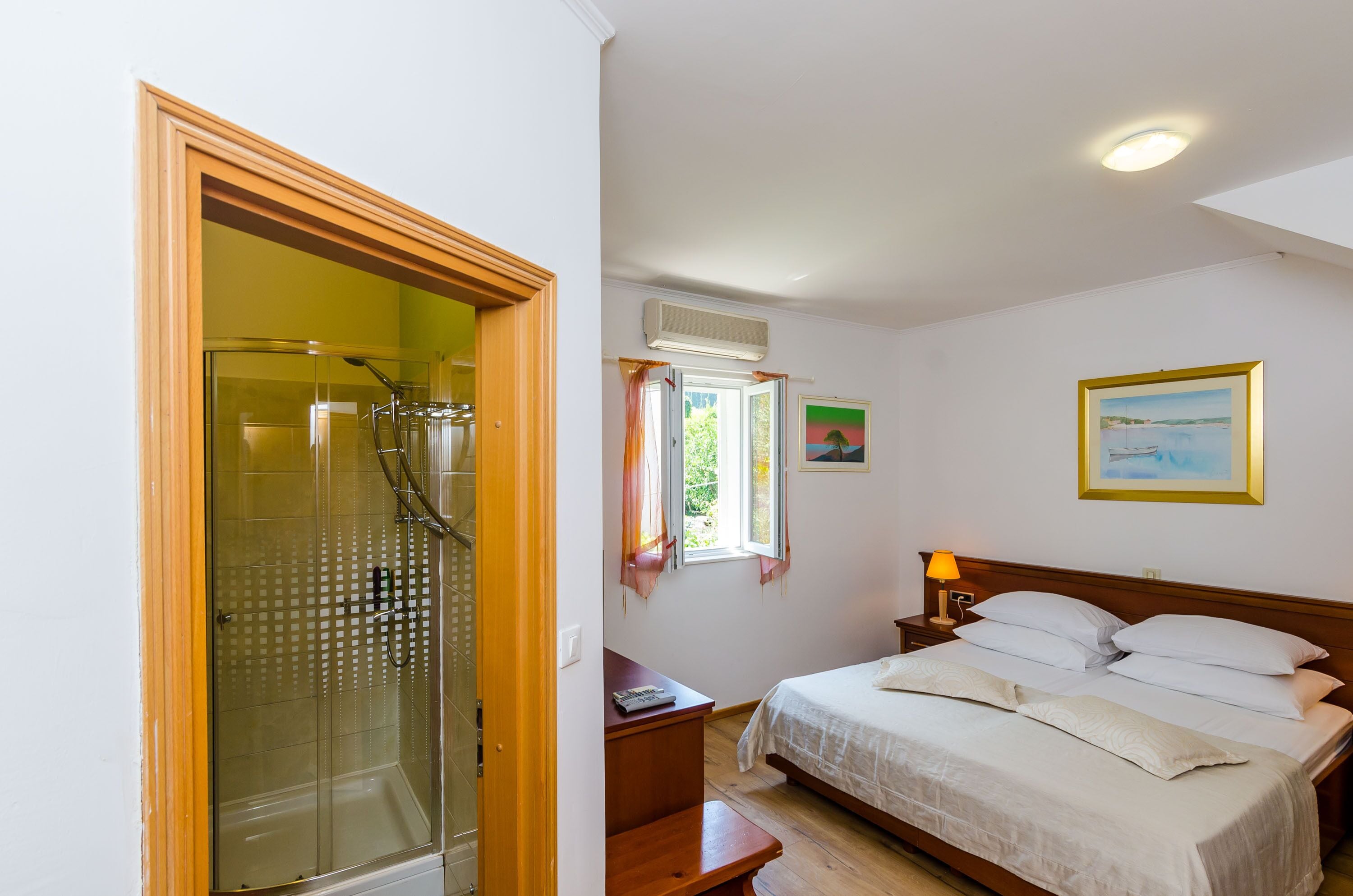 Quarto com cama, mesa de cabeceira, luminária e janela com cortinas.