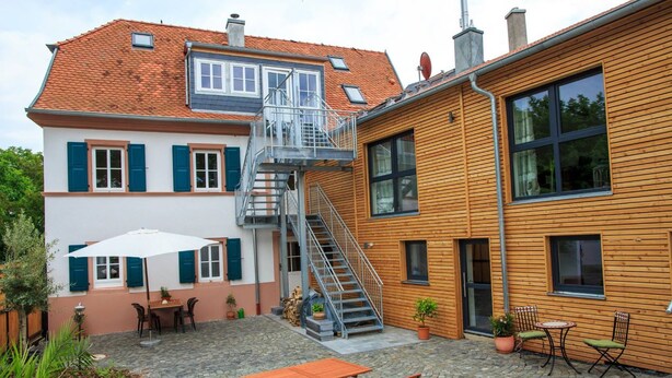 A two-story house with a wooden exterior, a stone-paved courtyard, and a metal staircase leading to the upper floor. - Winzerhaus am Eckbach (Bissersheim)