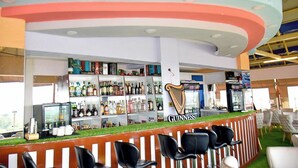 Una zona de bar con el logotipo de Guinness, estanterías llenas de botellas de licores y sillas negras.
