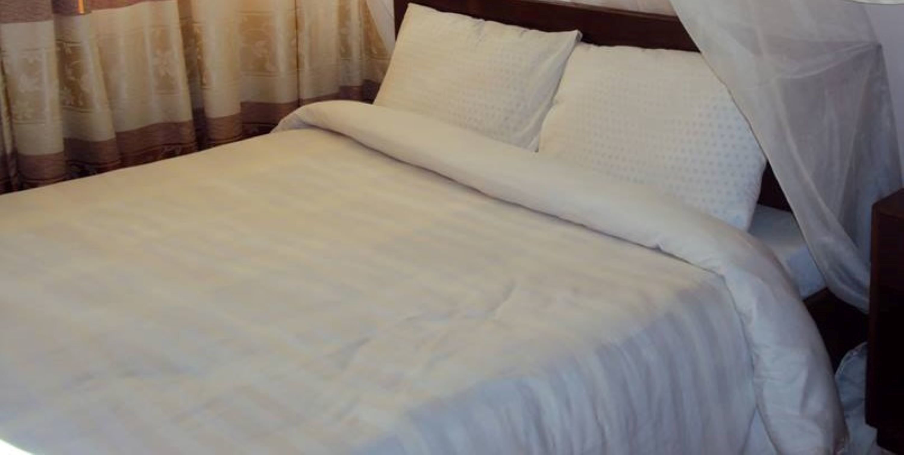 A neatly made bed with white bedding and a canopy.