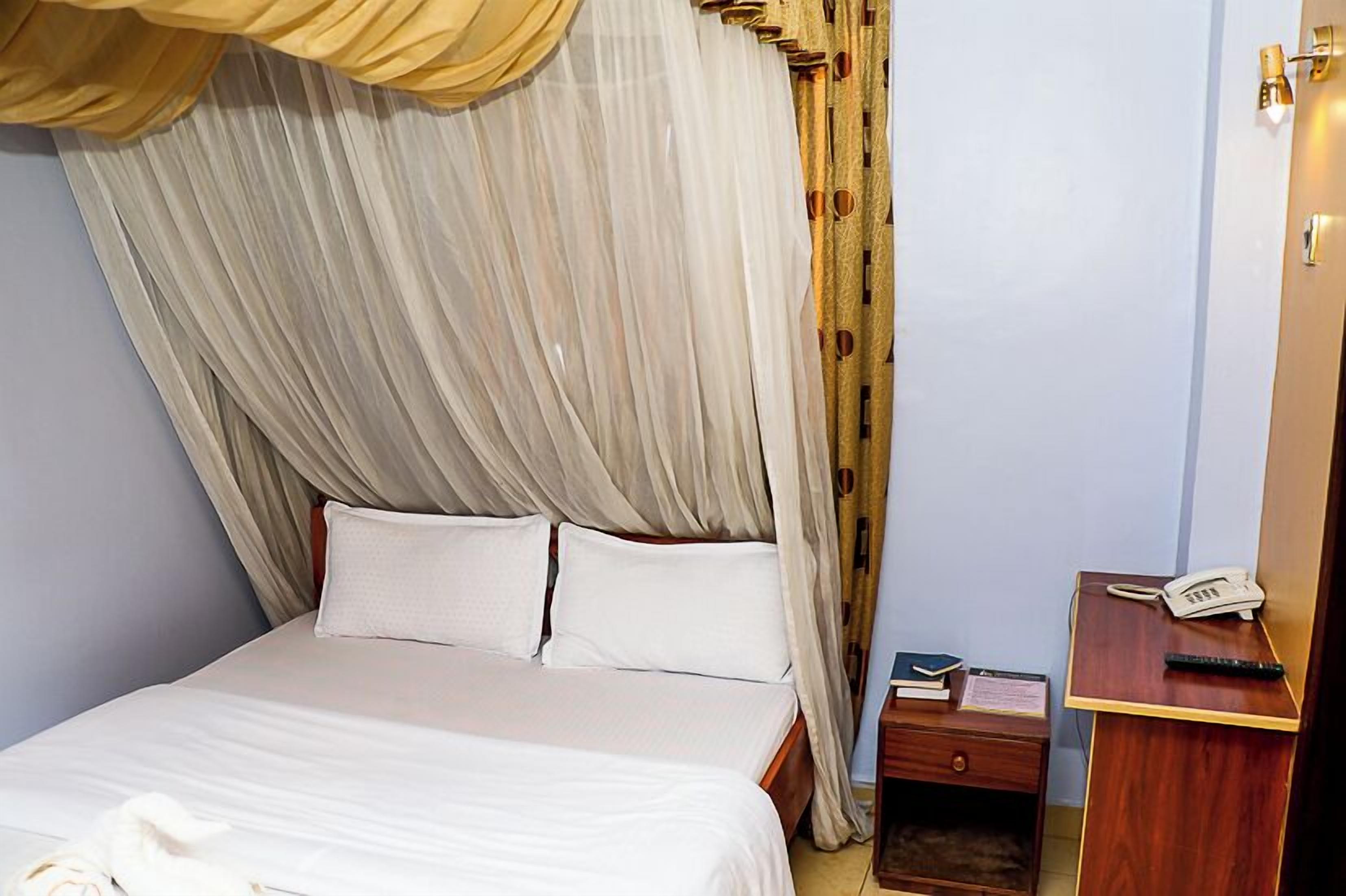 A hotel room with a bed, a nightstand, a telephone, and a desk with a chair.