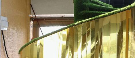 A room with a green artificial grass floor, a large mirror reflecting the room, and a window with blinds.