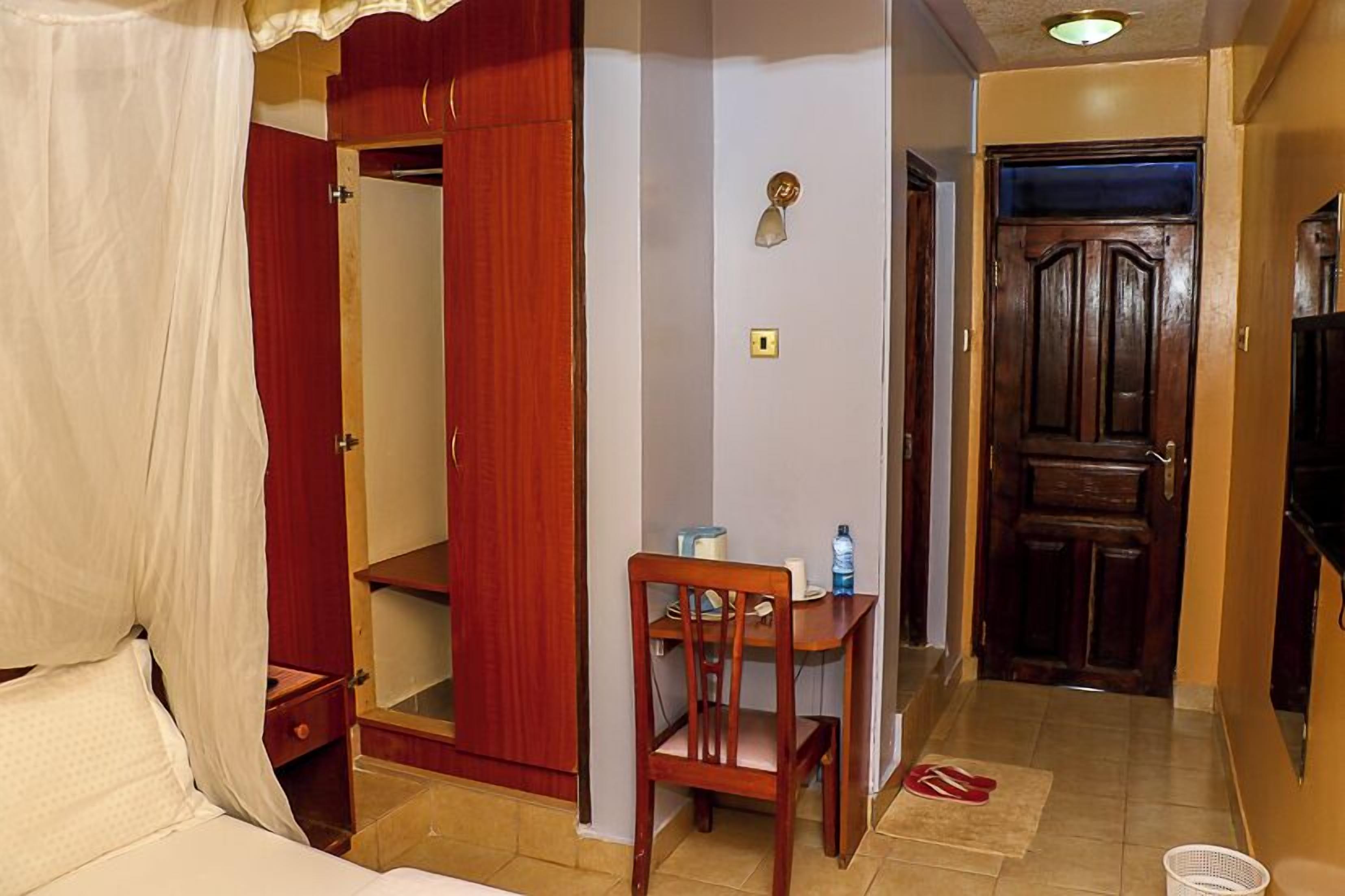 Habitación de hotel con cama, armario de madera, escritorio con silla y puerta que da a otra habitación.