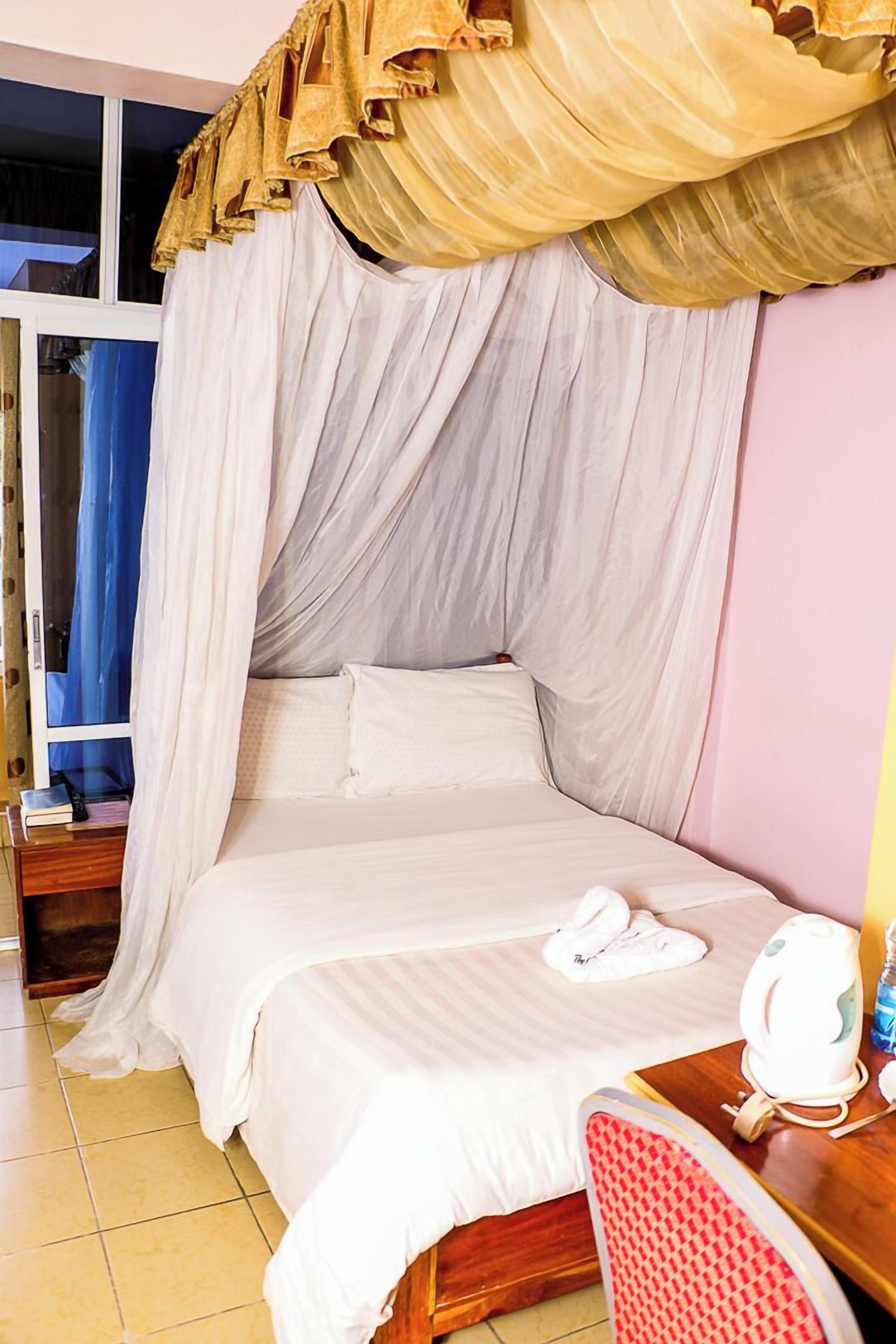 A room with a bed under a canopy, a bedside table with a lamp, and a chair.