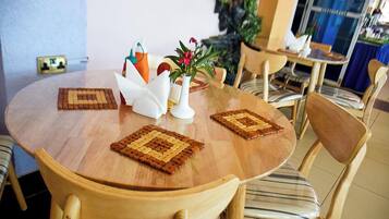 Ein runder Holztisch mit vier Stühlen, einer weißen Vase mit Blumen und zwei gewebten Untersetzern.