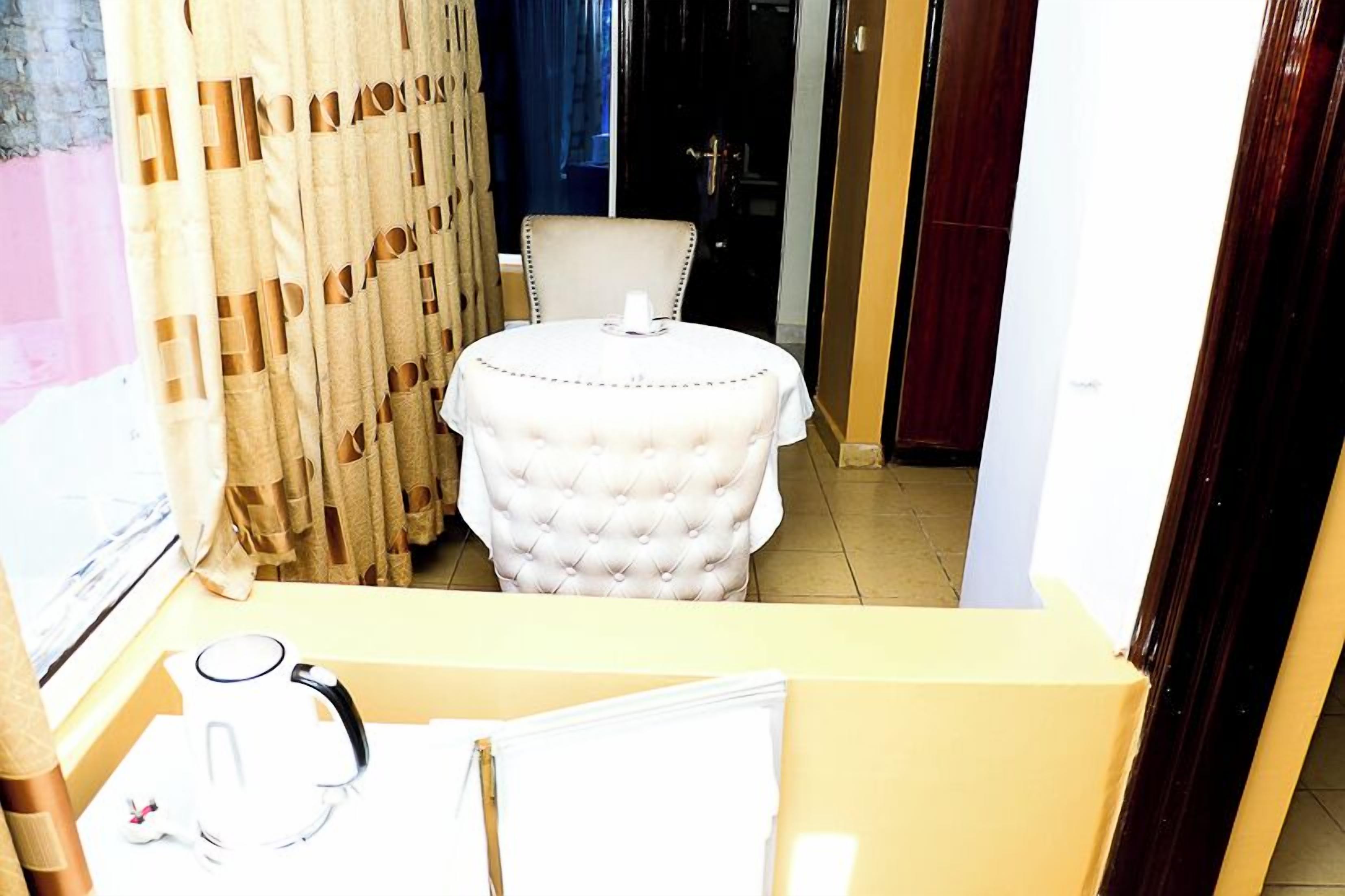 Ein Zimmer mit einem runden Tisch, einem Stuhl, einem Wasserkocher und einem Vorhang.