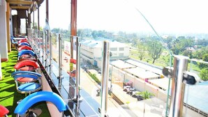 Una hilera de sillas rojas y azules a lo largo de un balcón con vista a un paisaje urbano.