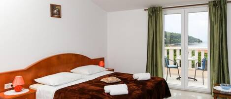 A hotel room with a large bed, a nightstand, a lamp, and a view of the outdoors through a sliding glass door.