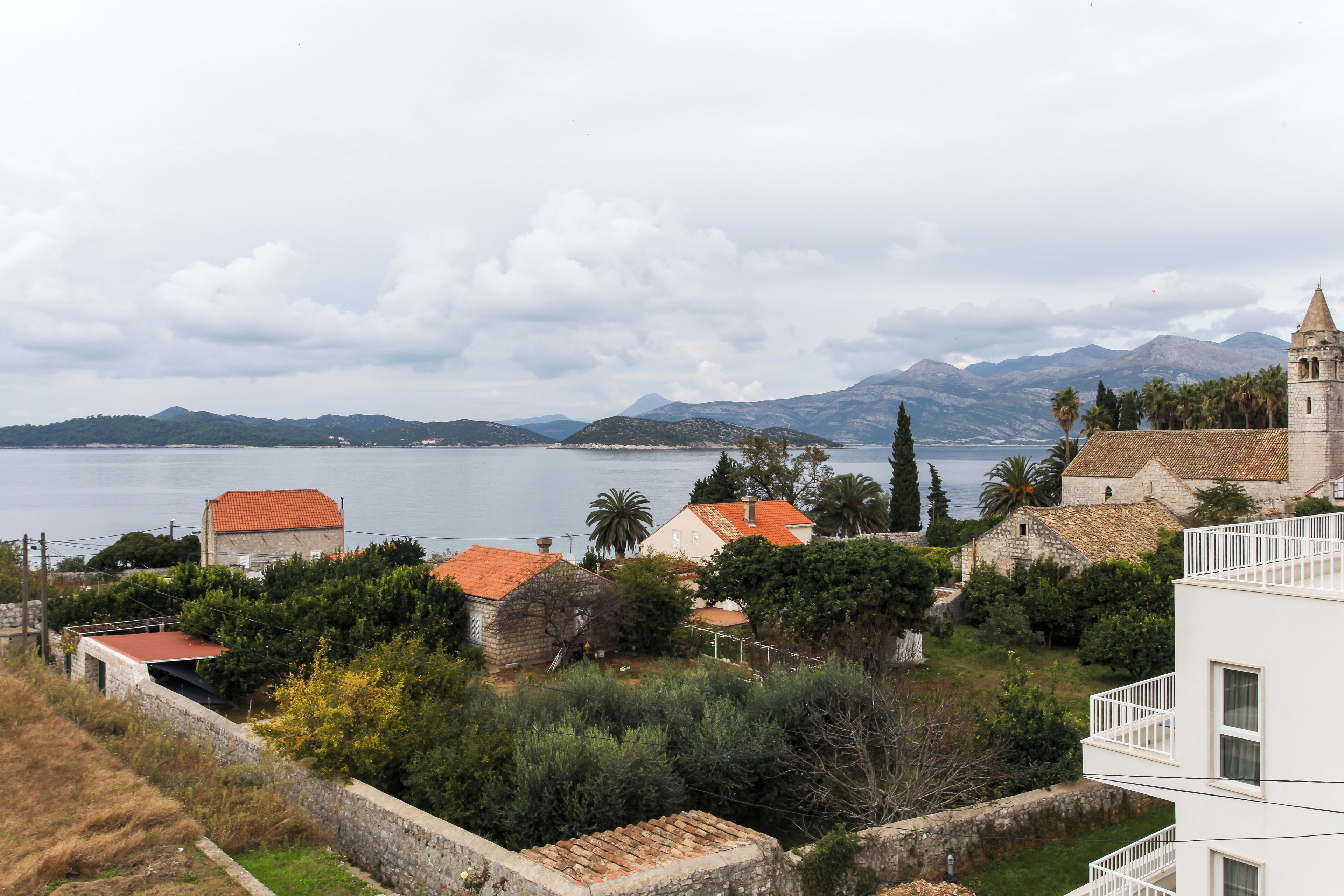 A coastal village with traditional stone buildings, a church, and a view of the sea and mountains.