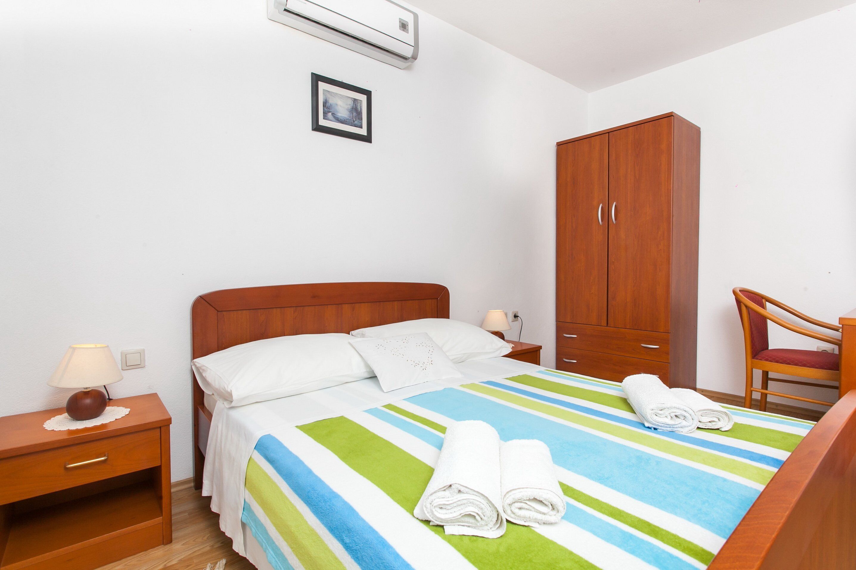 Hotellihuone, jossa on sänky, puinen vaatekaappi, yöpöytä ja tuoli.