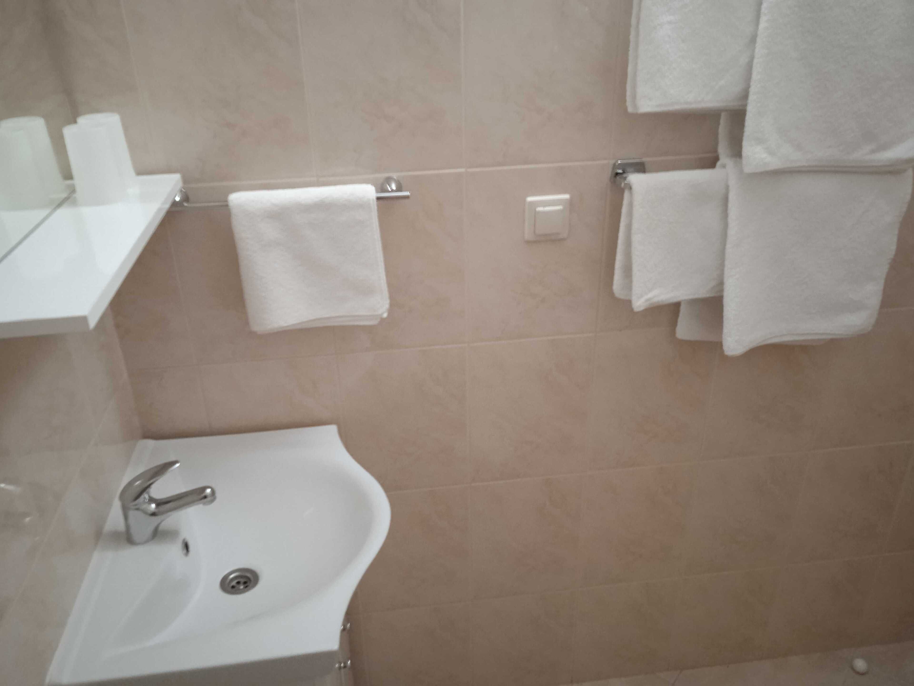 A bathroom with a sink, a towel rack with multiple towels, and a toilet paper holder.