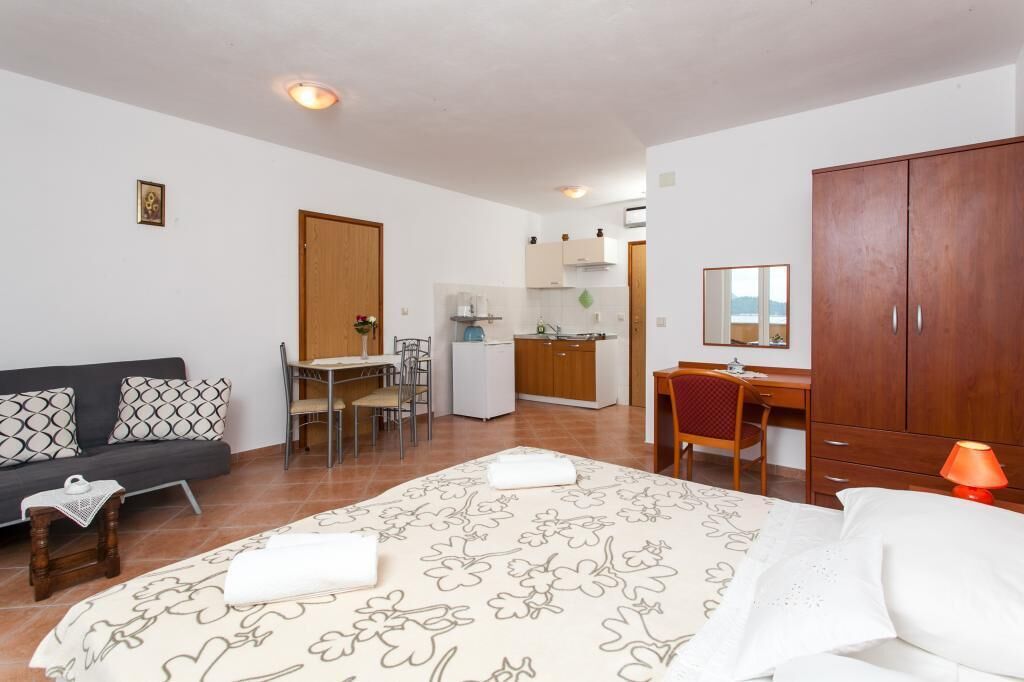 Ein kompaktes Hotelzimmer mit Bett, Schreibtisch, Küchenzeile und Kleiderschrank.