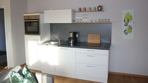 Una cocina moderna con armarios blancos, horno empotrado, cafetera y tabla de cortar de madera.